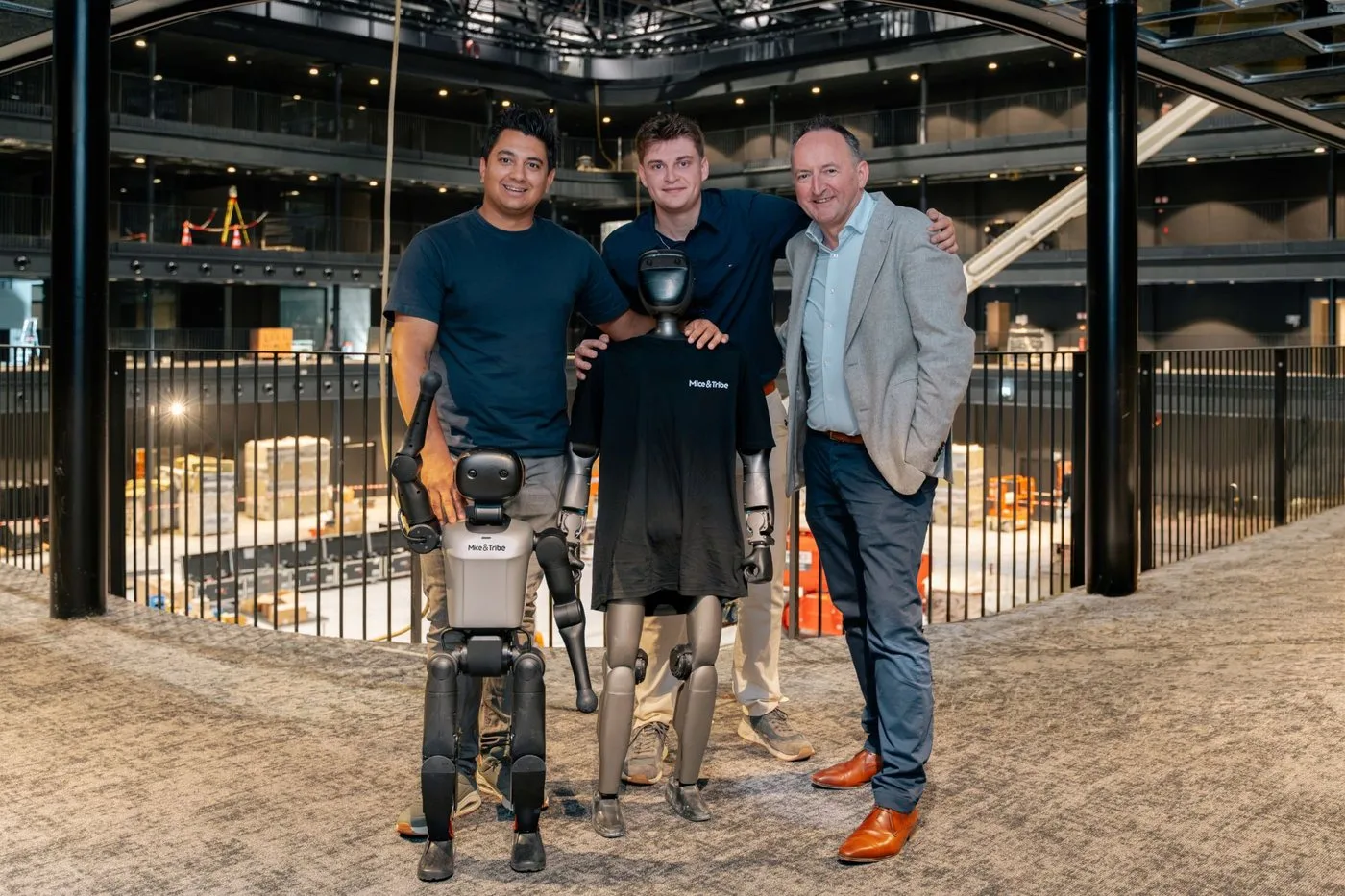 Robin Paesen, Leandro Ketelslegers en Bart Koninckx met twee humanoïde robots, één in een Mice & Tribe T-shirt