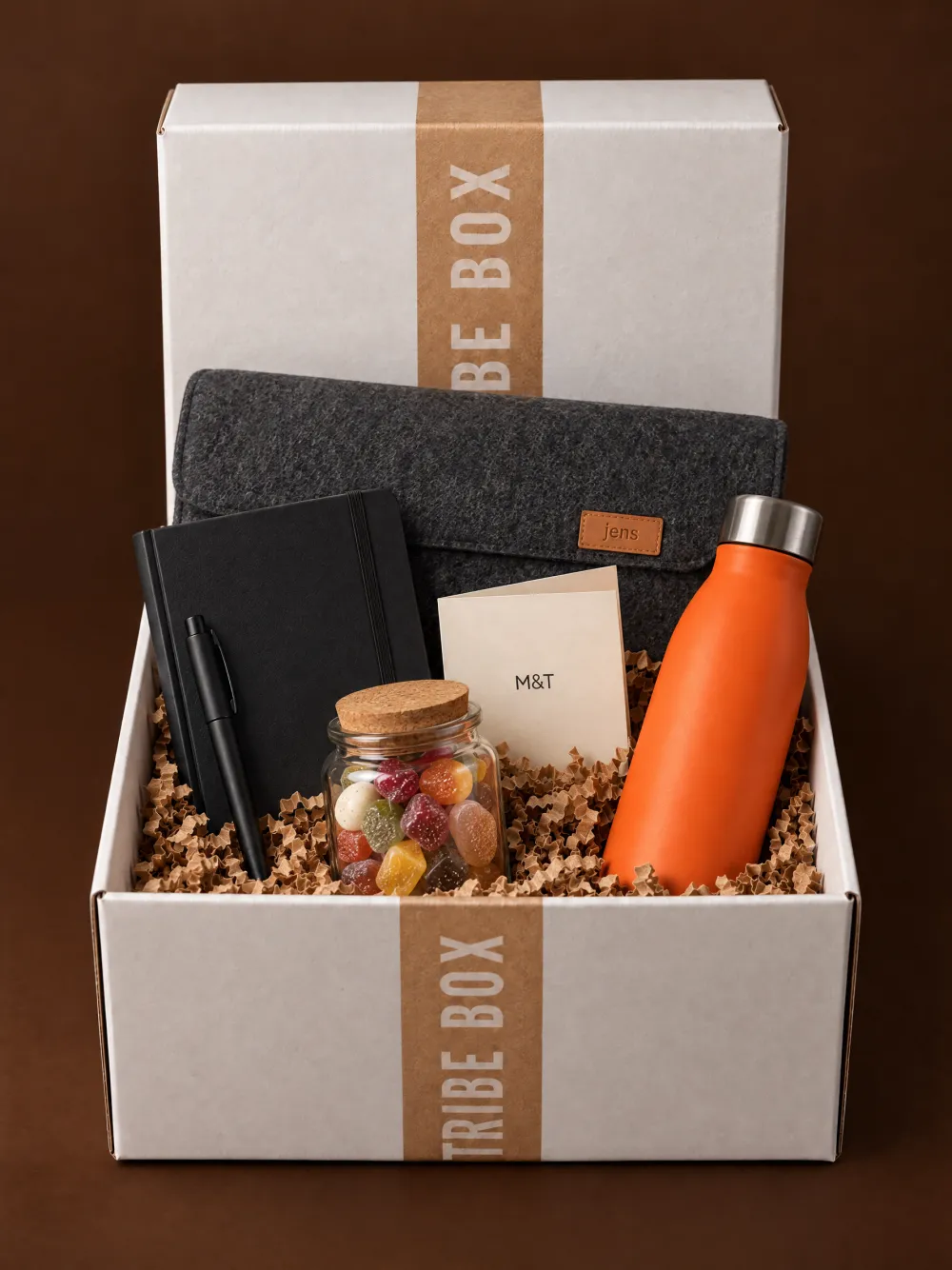 Een open Tribe Box met een laptophoes met naamlabel, een notitieboek, een pen en een oranje drinkfles