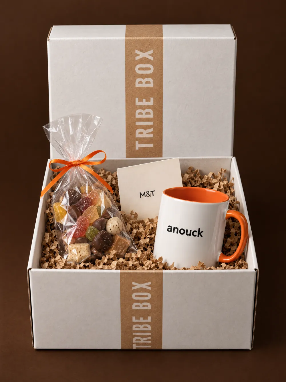 Een open Tribe Box met een witte tas met oranje binnenkant en de naam Anouck, een zakje snoep en een kaartje